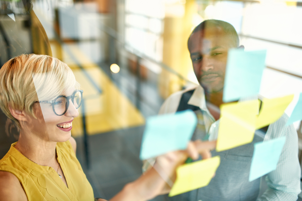 Two creative millenial small business owners working on social media strategy brainstorming using adhesive notes in windows Two creative millenial small business owners working on social media strategy brainstorming using adhesive notes in windows